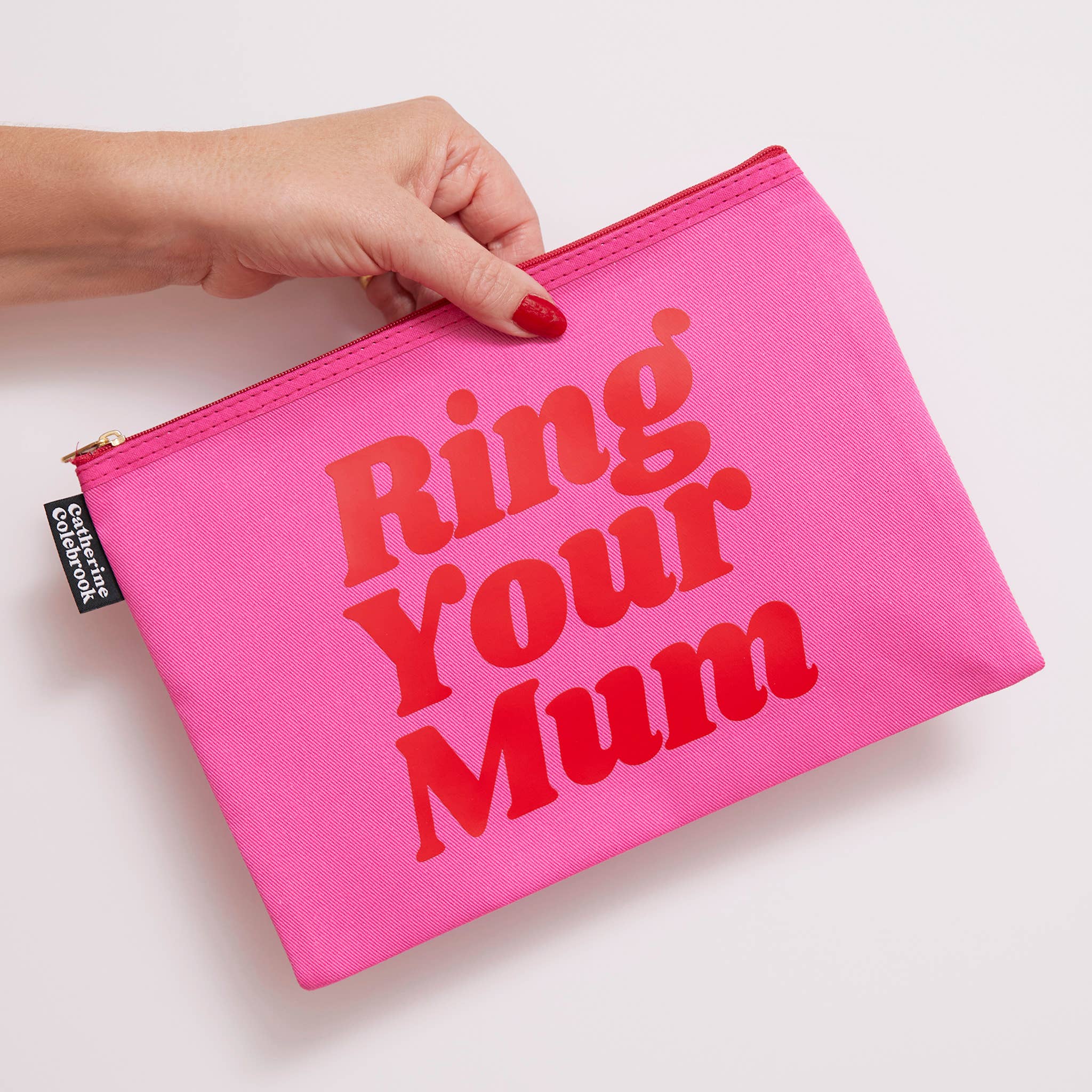Pink pouch with 'Ring Your Mum' text held by a hand on a light background