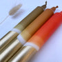 Three cylindrical candles with gold, orange, and red colors on a white background.