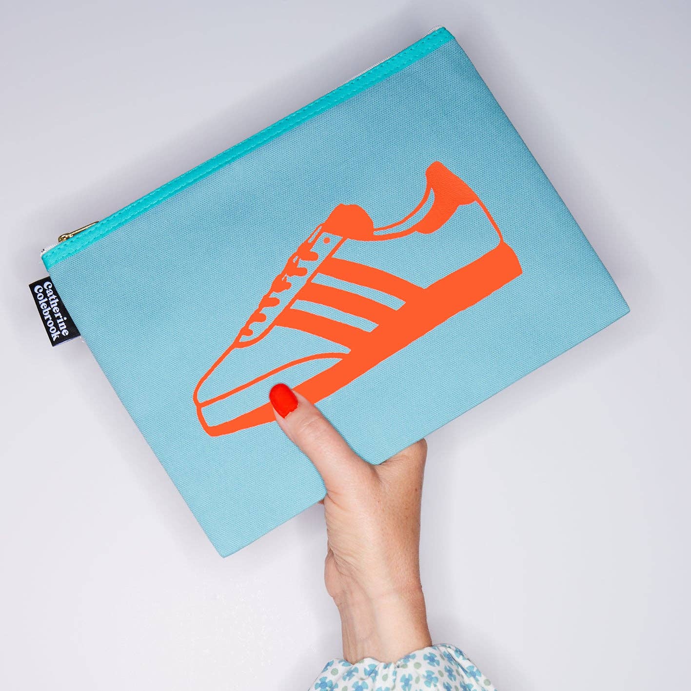 Light blue pouch with orange sneaker design held by a hand on a light gray background