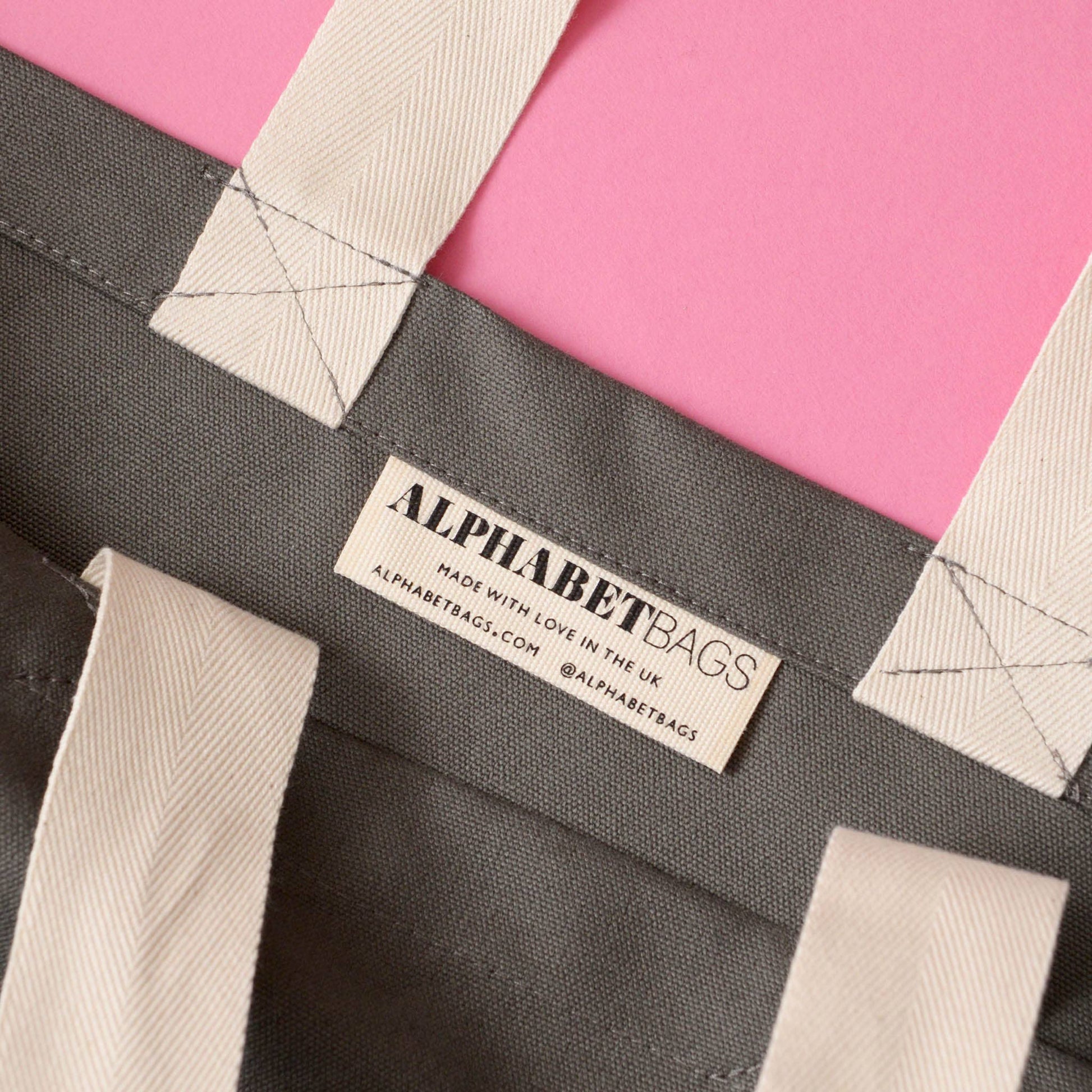 Gray tote bag with 'Alphabet Bags' label on a pink background
