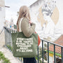 Person holding a green tote bag with text, standing on a balcony with a mural in the background.