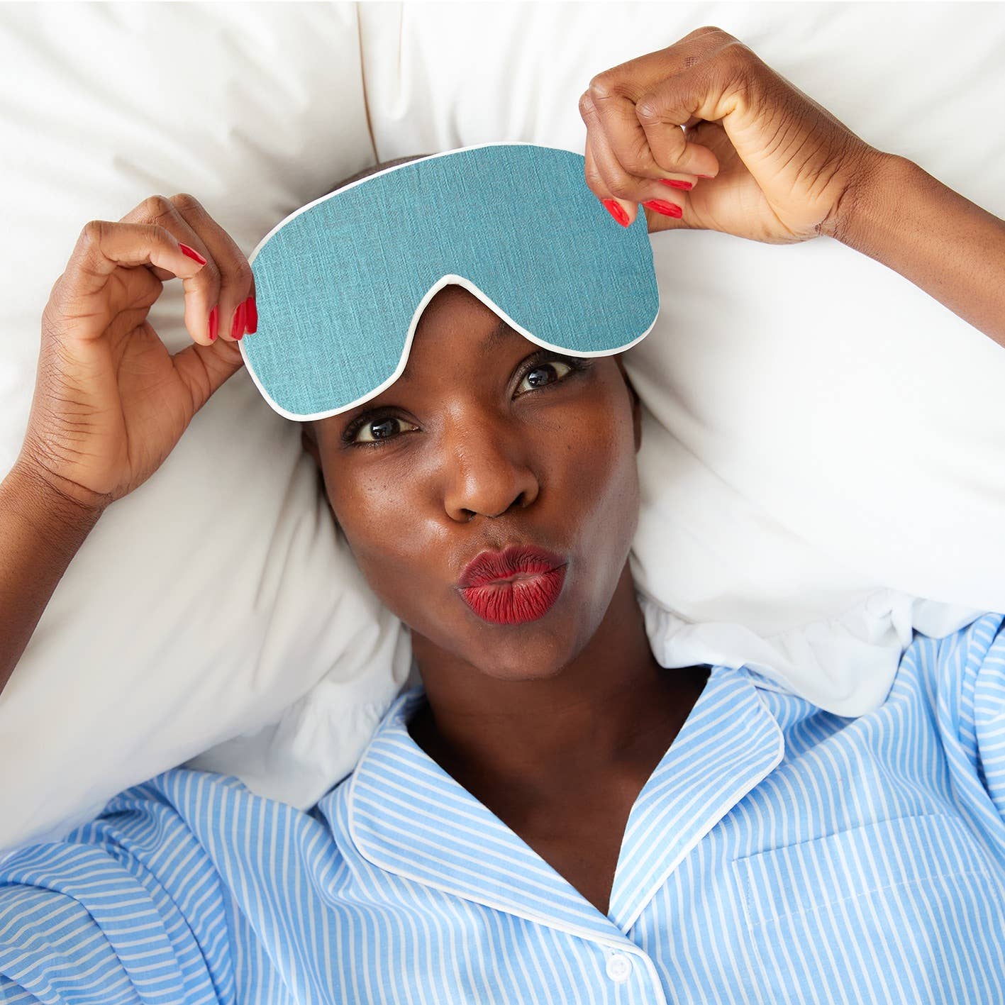 Woman wearing a blue sleep mask with a white pillow behind her head.