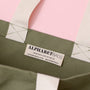Close-up of a green tote bag with 'Alphabet Bags' label on a pink background