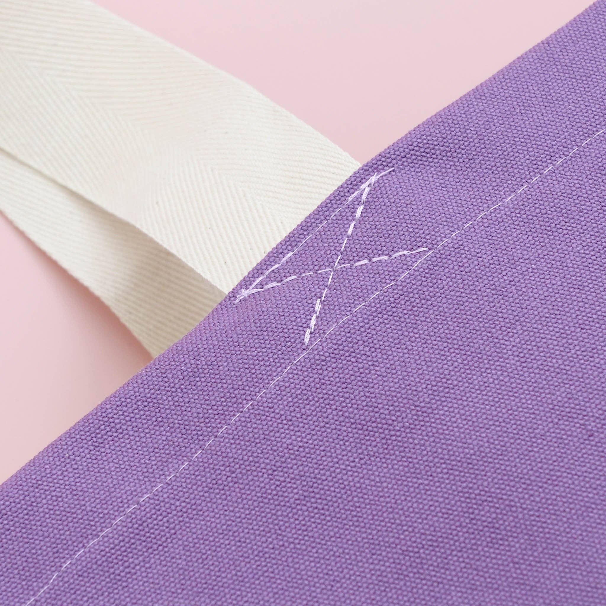 Close-up of a purple fabric with white stitching on a pink background