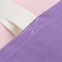 Close-up of a purple fabric with white stitching on a pink background