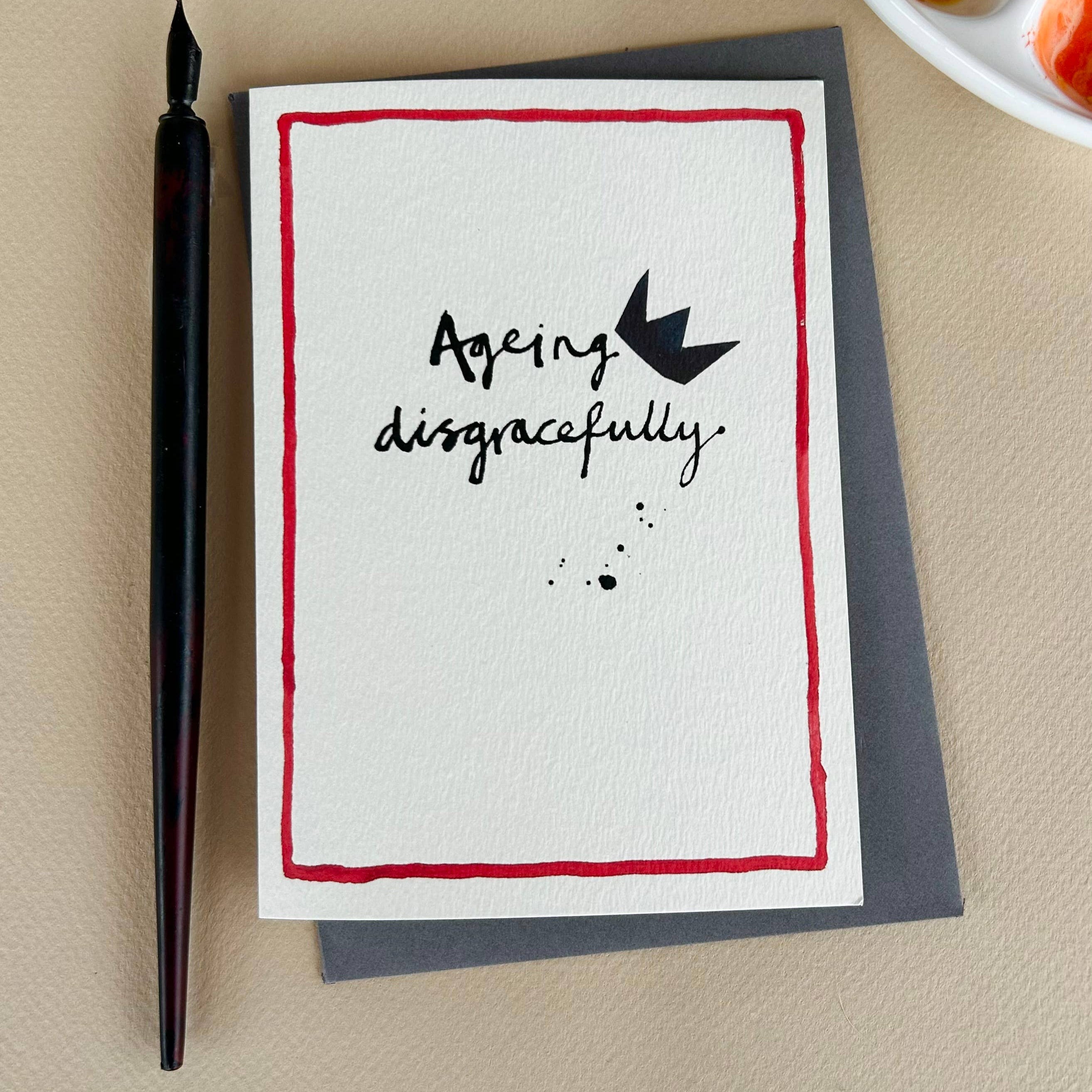 Card with 'Ageing disgracefully' text and a pen on a beige surface