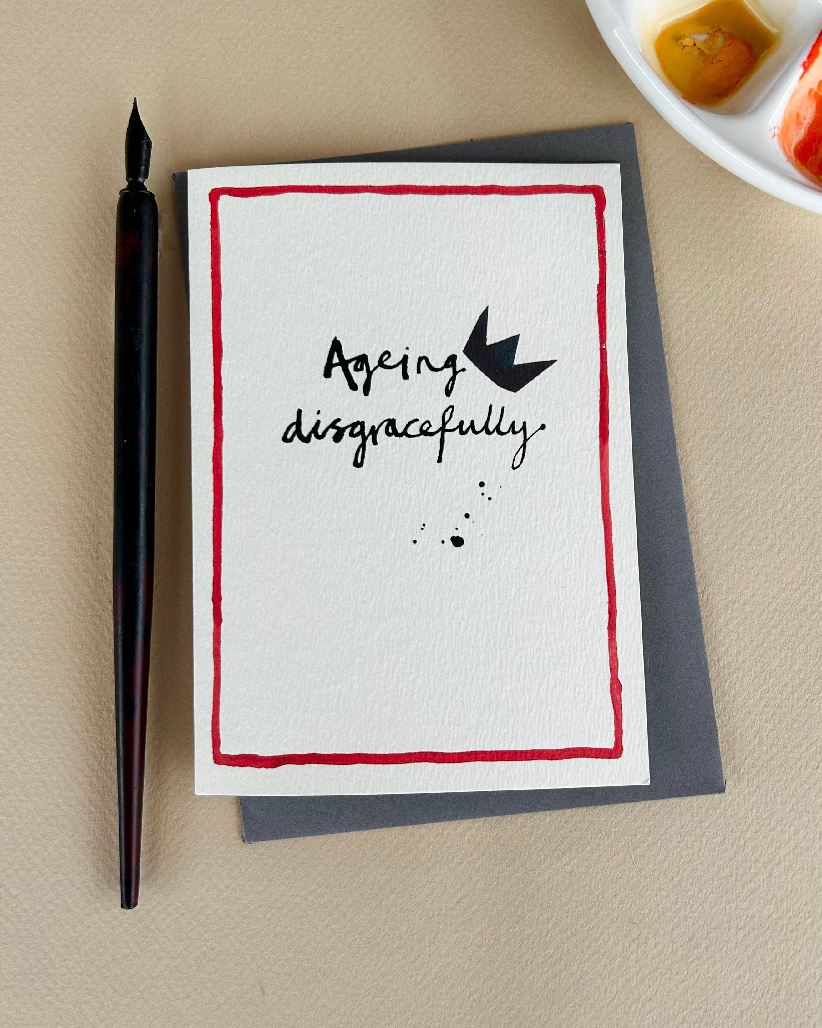 Card with 'Ageing disgracefully' text and a pen on a beige surface