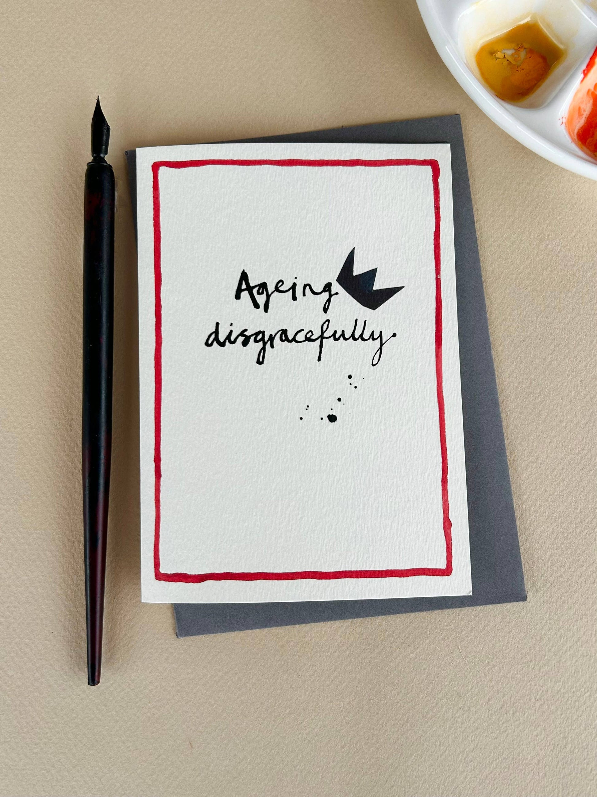 Card with 'Ageing disgracefully' text and a pen on a beige surface