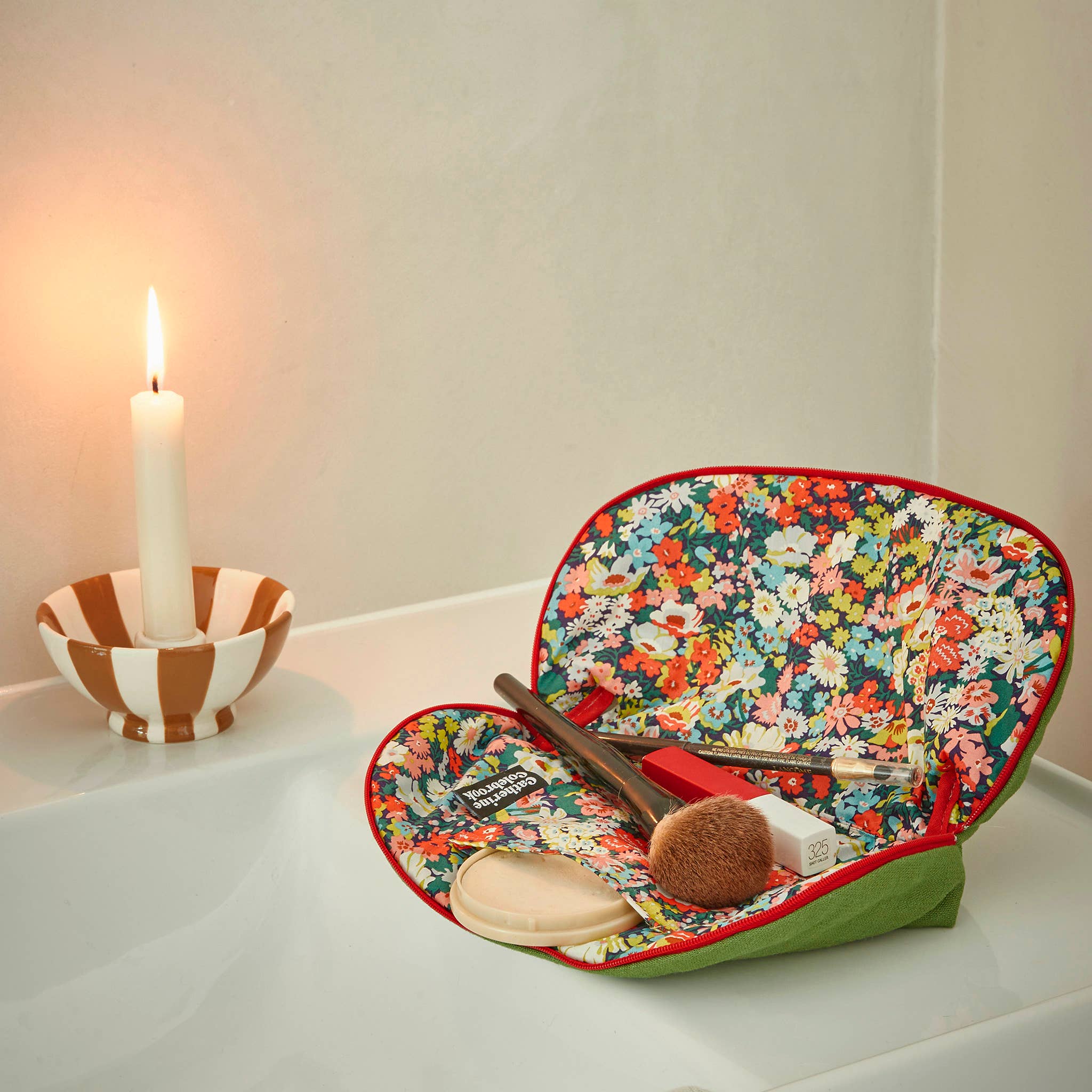 Makeup case with floral design on a white surface next to a lit candle.