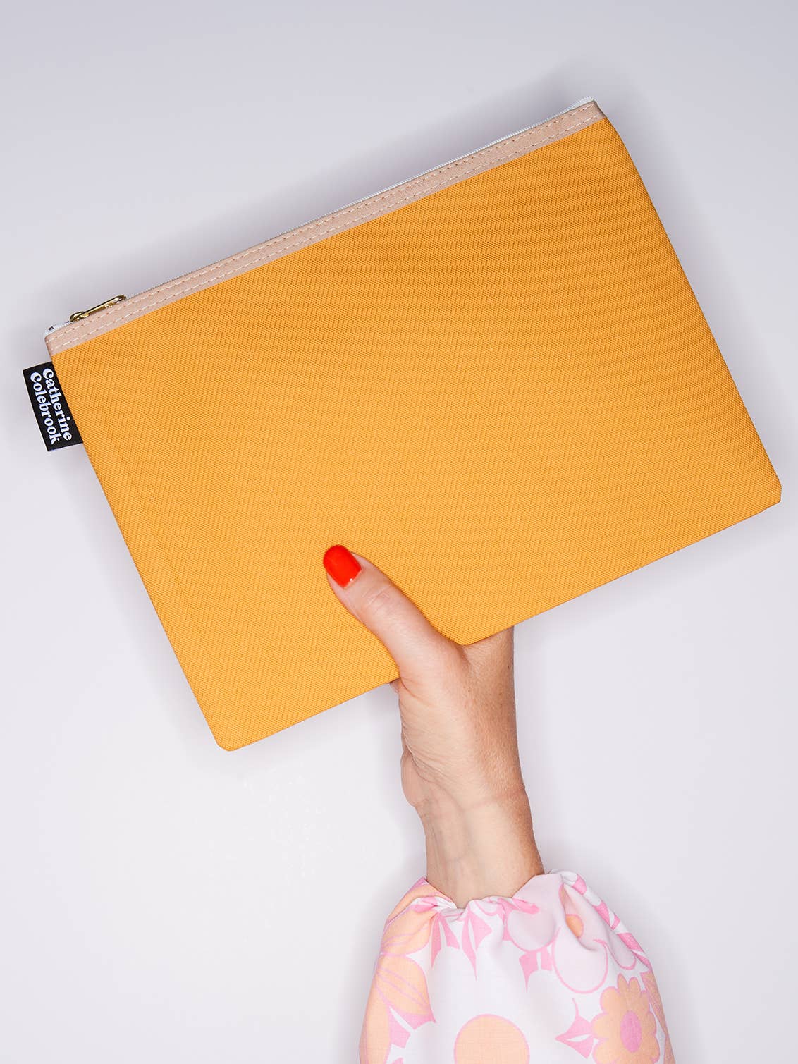 Yellow pouch held by a hand with red nail polish on a light gray background