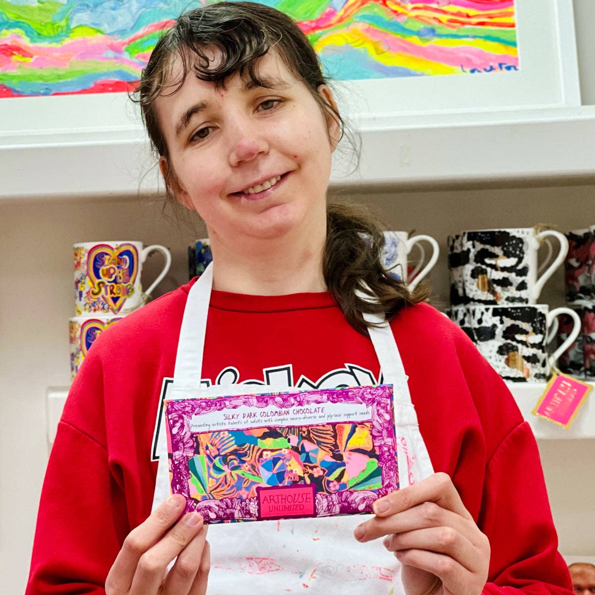 Person holding a craft kit in a colorful room with shelves of mugs and art supplies.