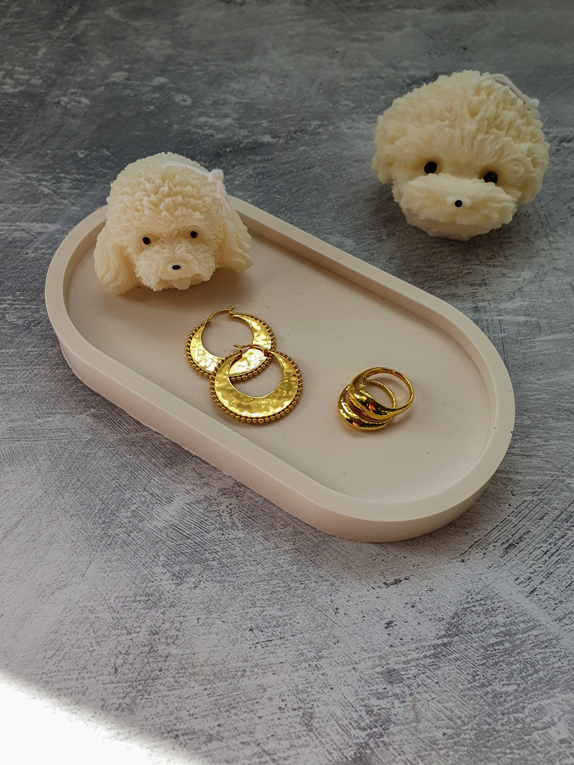 Two small plush poodles and gold rings on a beige tray with a gray background