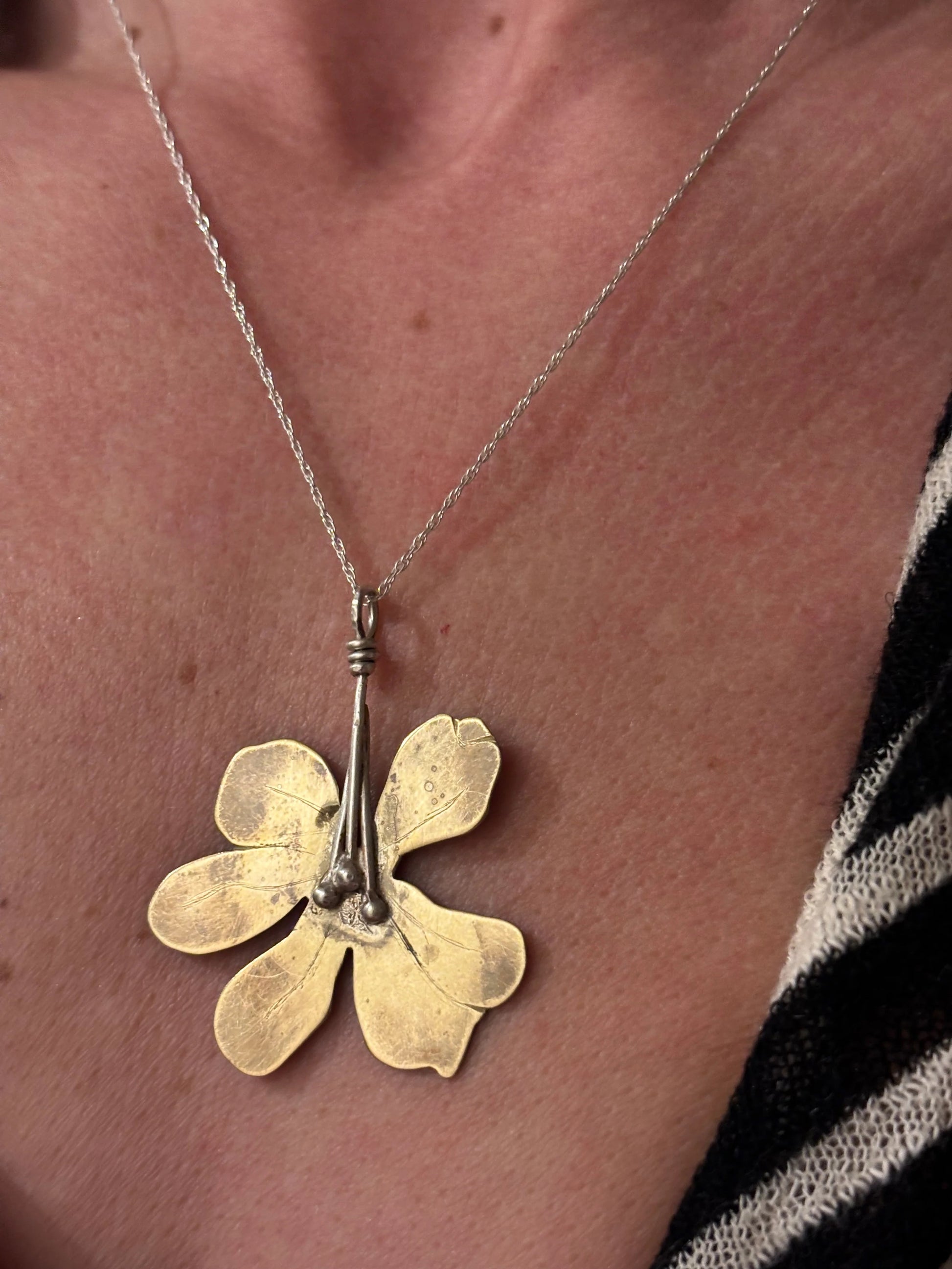 Gold flower-shaped pendant on a chain worn around the neck.