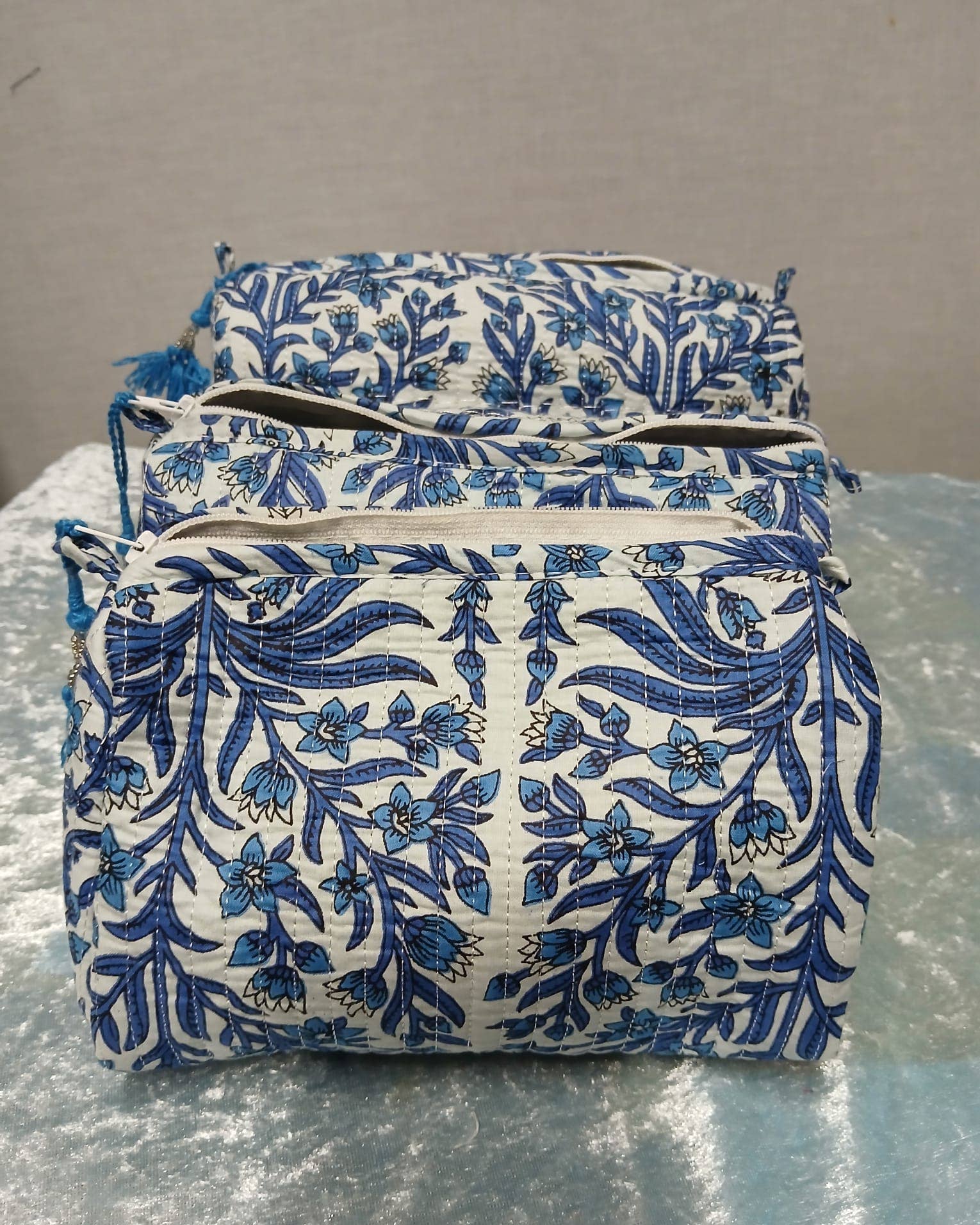 Set of three blue floral-patterned pouches on a reflective surface with a neutral background