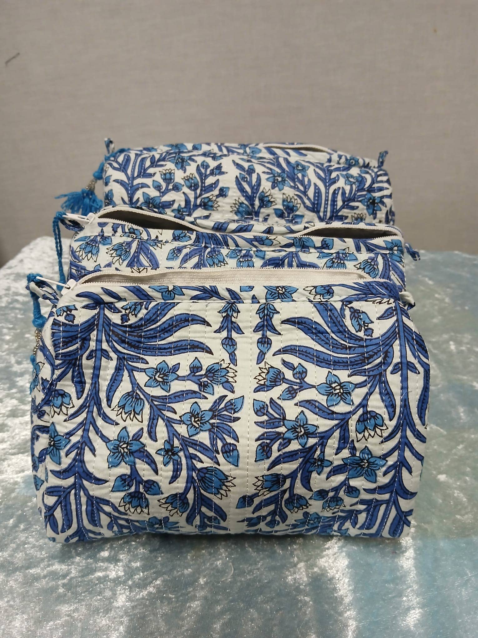 Set of three blue floral-patterned pouches on a reflective surface with a neutral background
