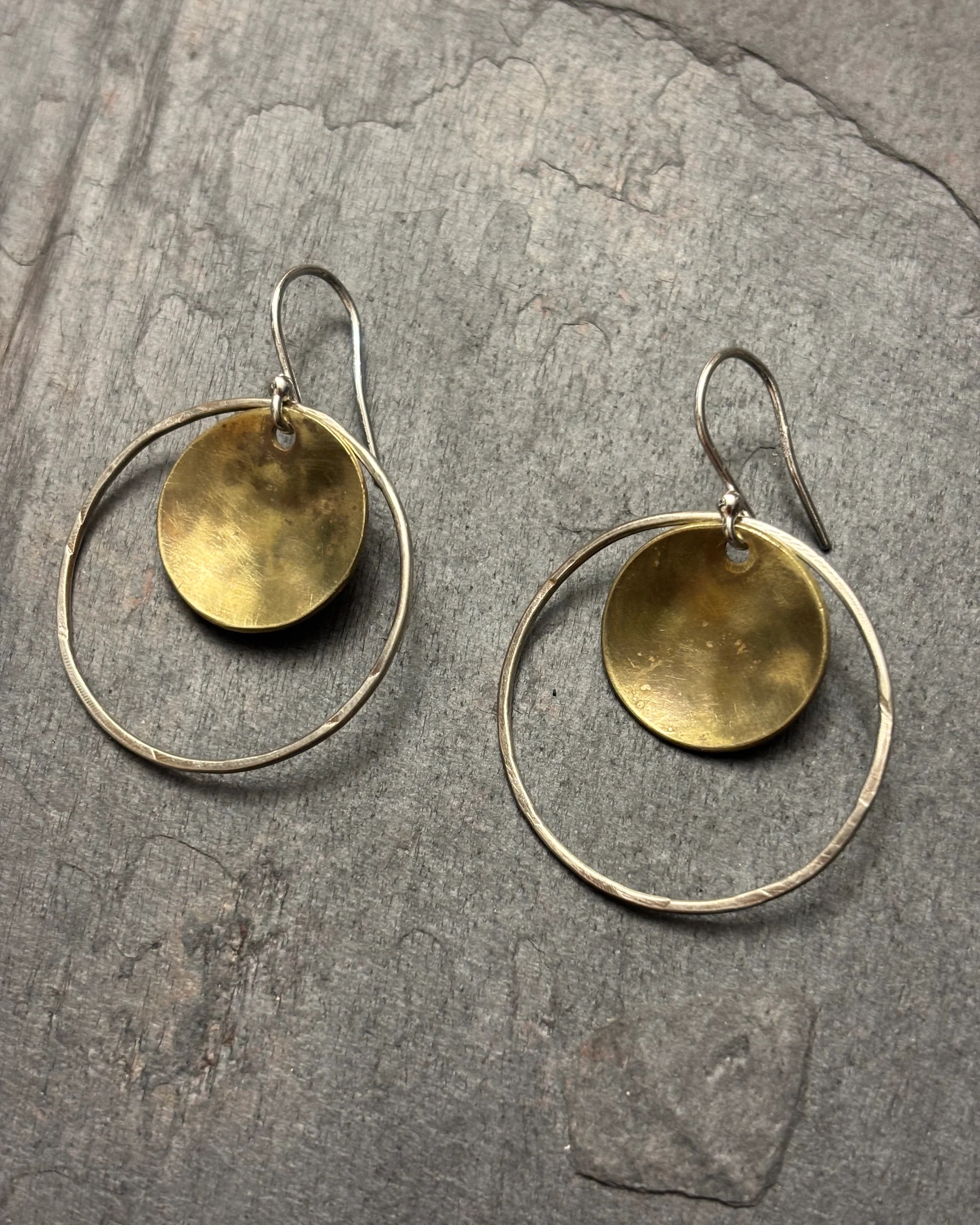 Pair of gold and silver hoop earrings on a stone surface