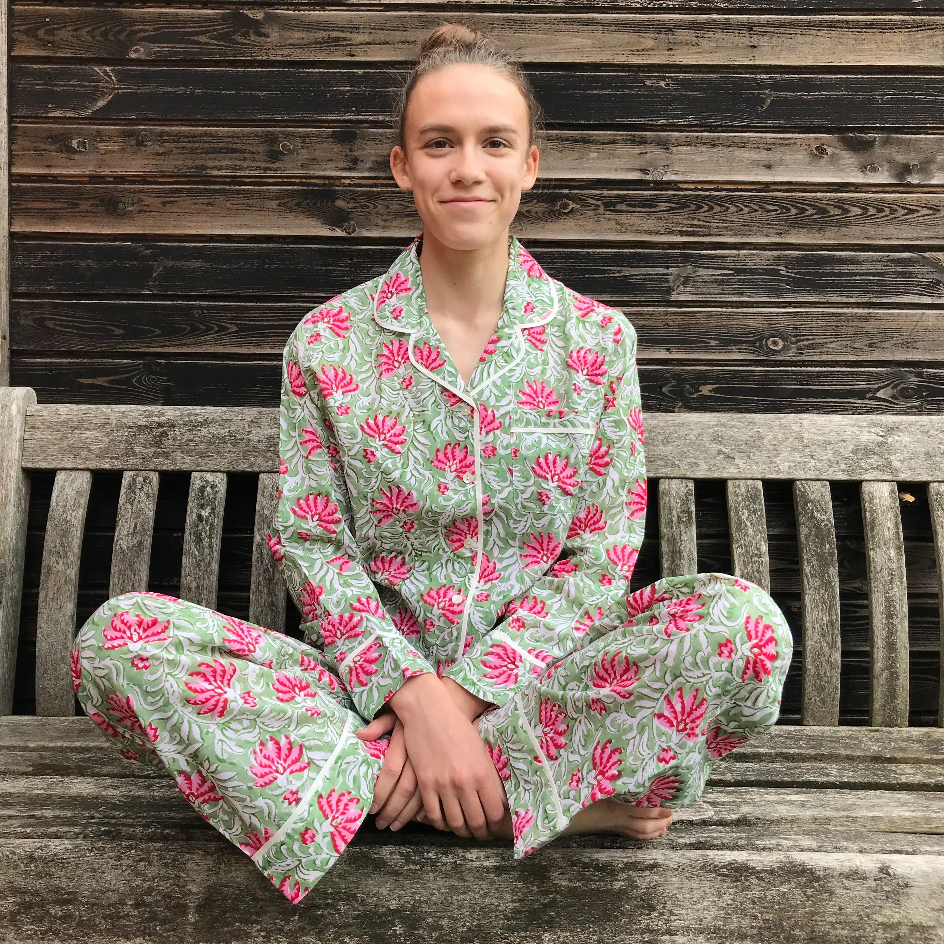 Person wearing a green and pink floral pajama set sitting on a wooden bench.