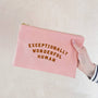 Pink pouch with 'Exceptionally Wonderful Human' text held by a hand on a light background