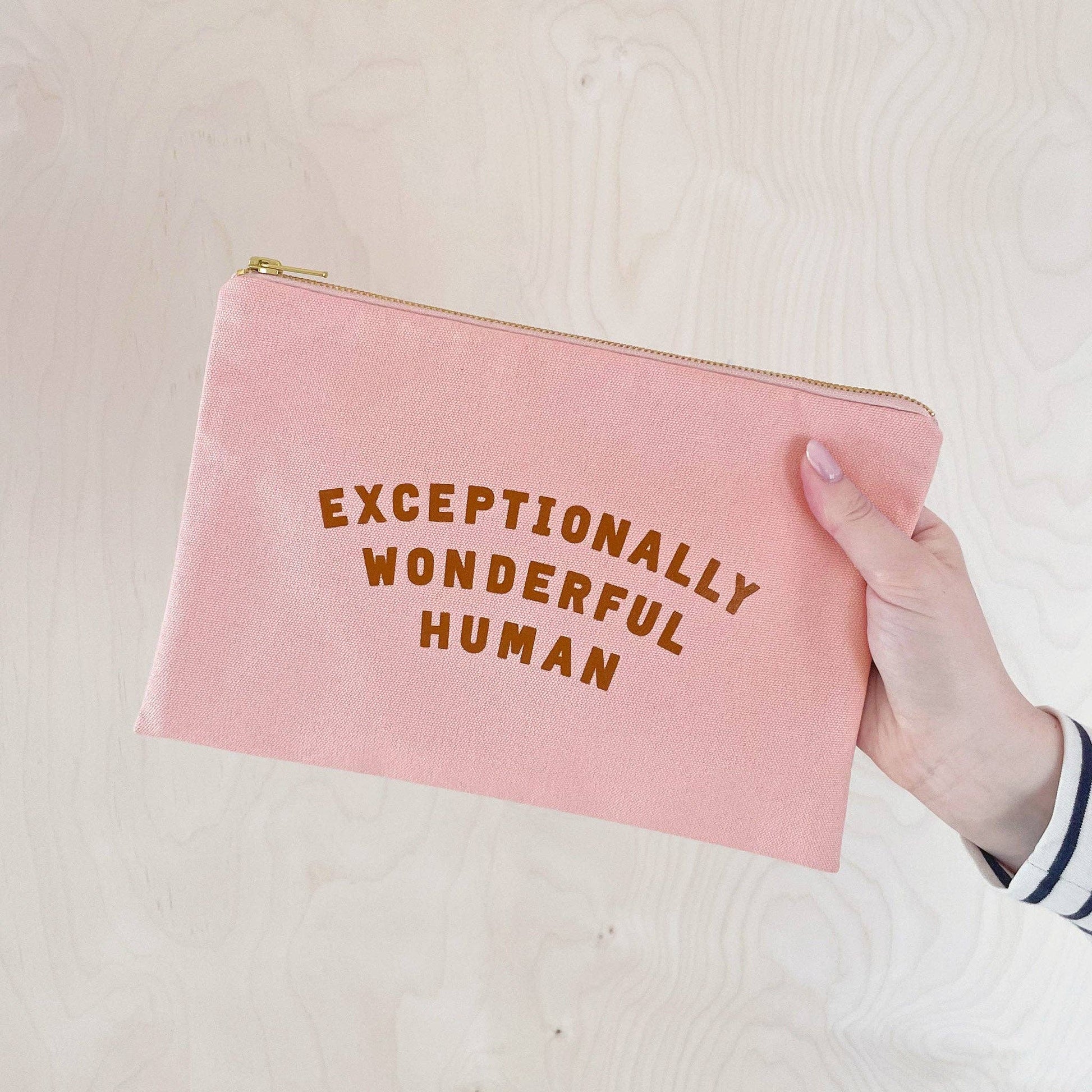 Pink pouch with 'Exceptionally Wonderful Human' text held by a hand on a light background