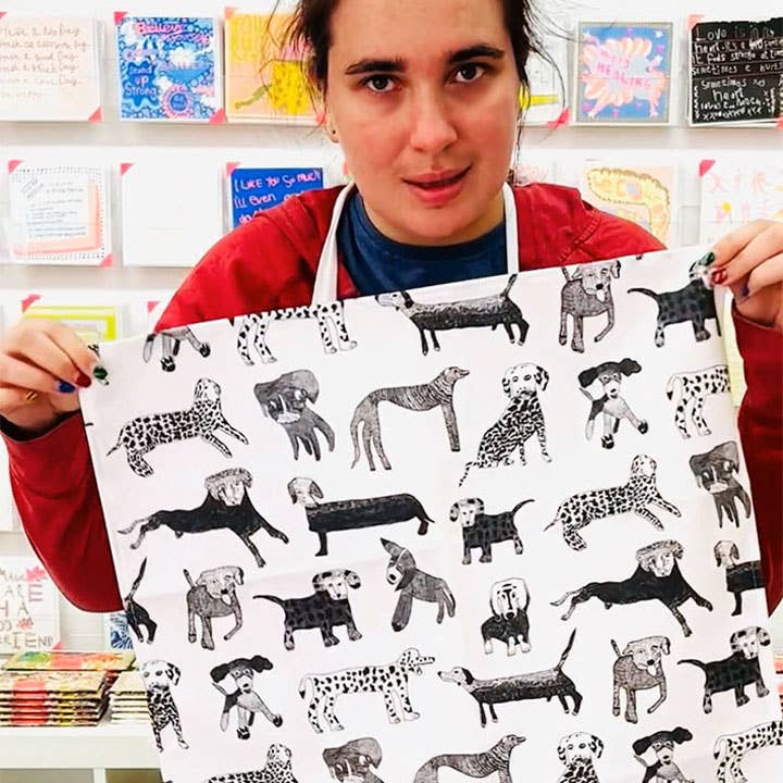 Person holding a large piece of paper with black and white dog illustrations in front of a colorful wall.