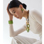 Woman wearing a long necklace and green earrings against a white background