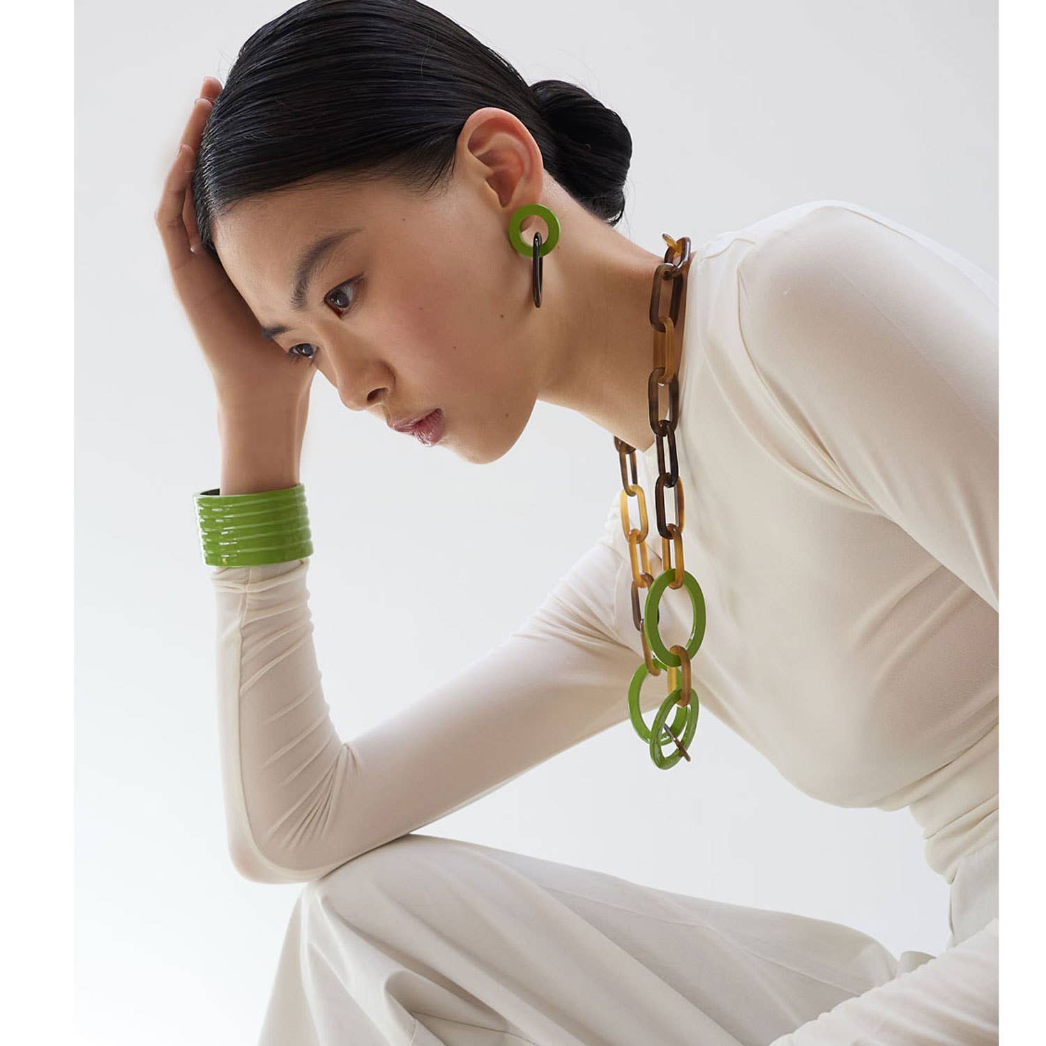 Woman wearing a long necklace and green earrings against a white background