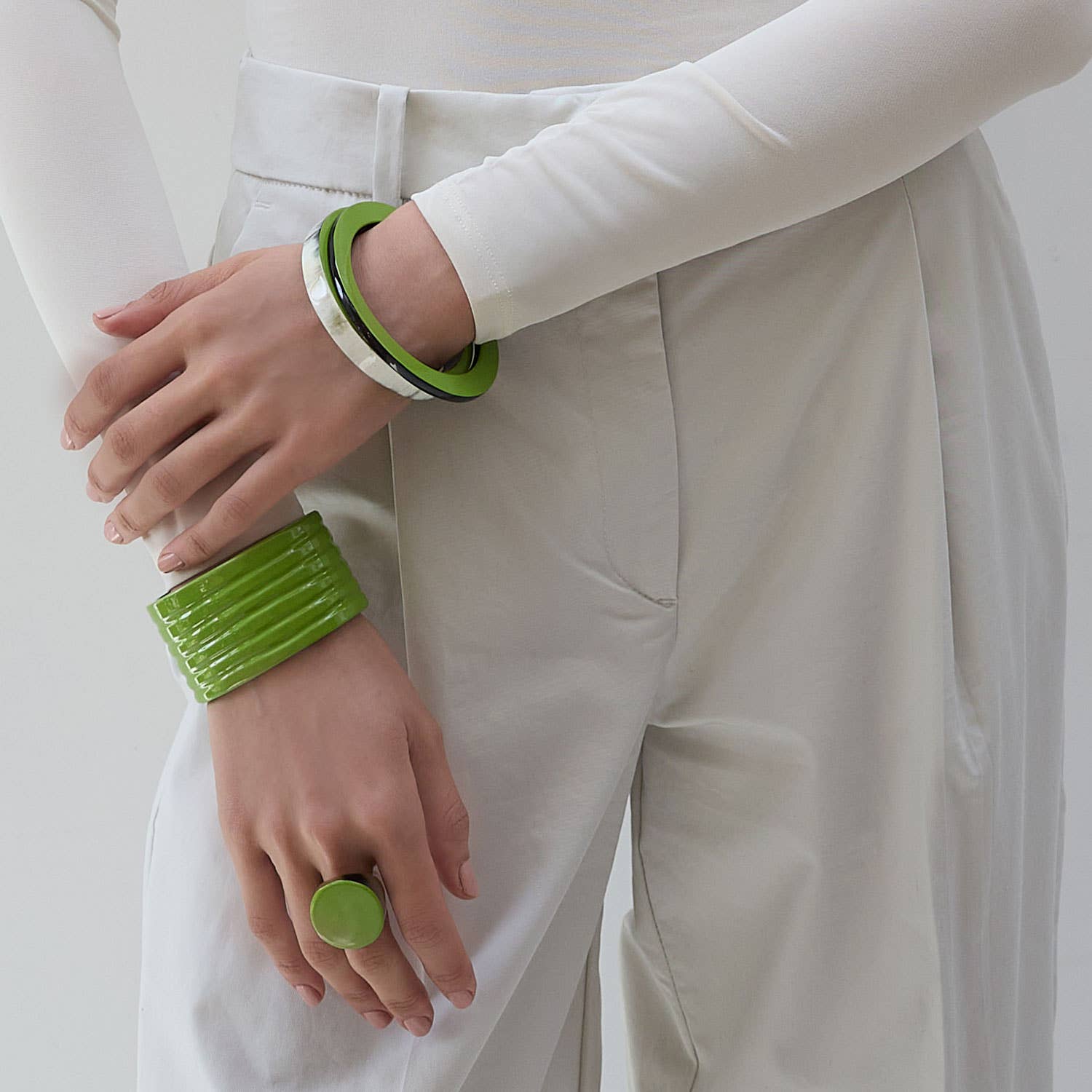 Person wearing green bracelets and a ring on a plain background