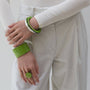 Person wearing green bracelets and a ring on a plain background