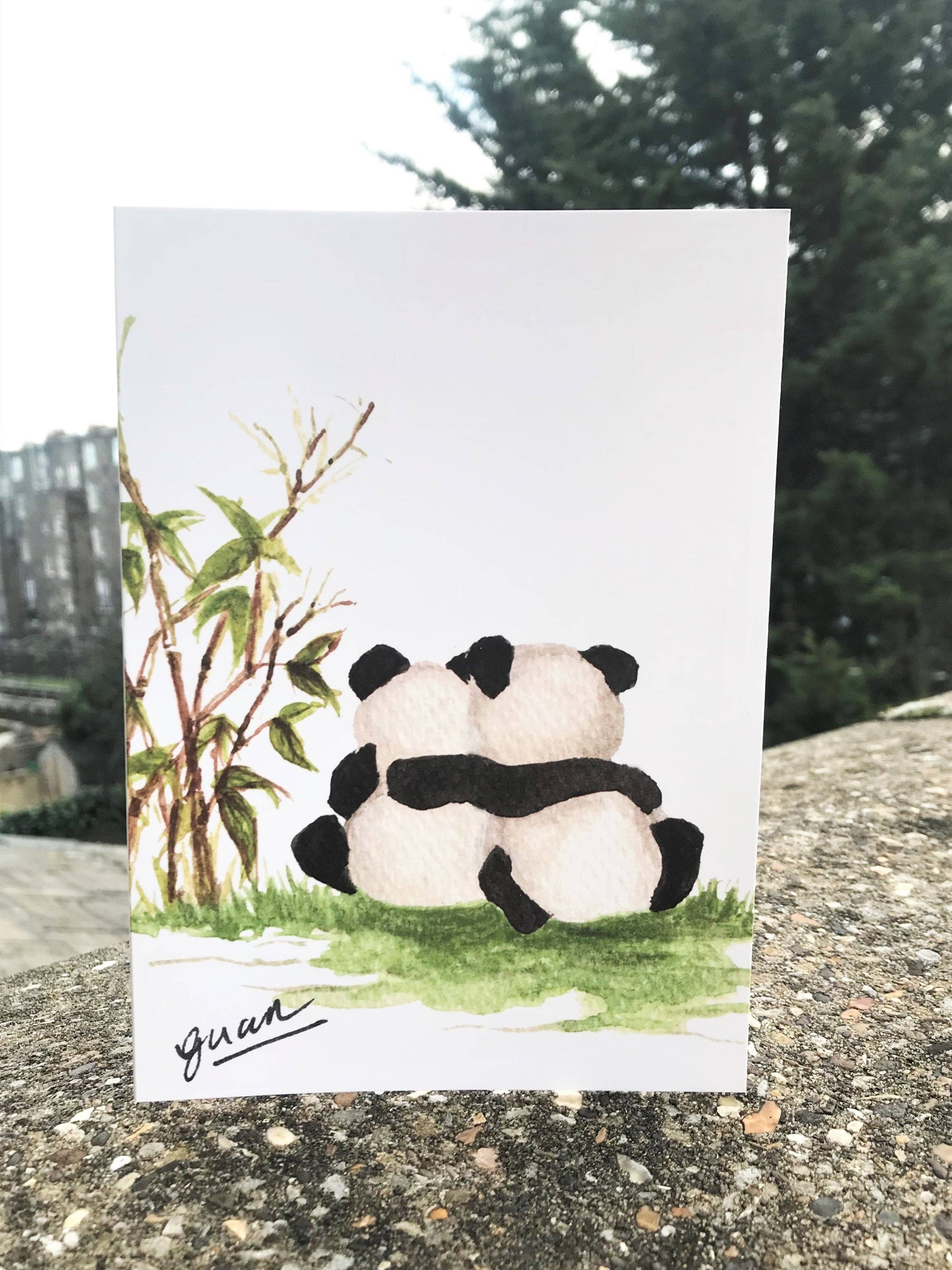 Card with two panda bears hugging and bamboo plants on a natural background