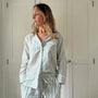 Woman wearing a light gray pajama set with a subtle pattern against a white door background.