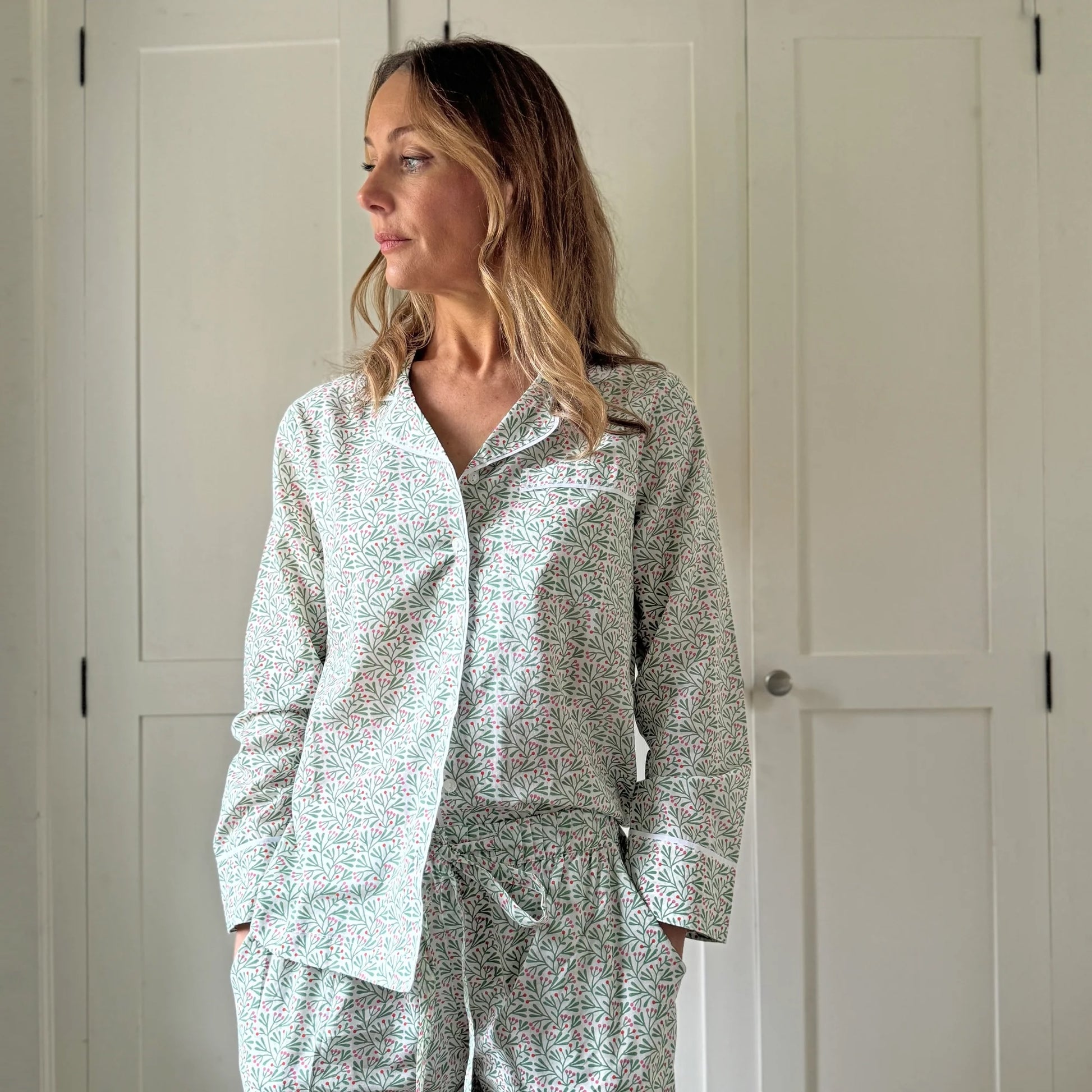 Woman wearing a light gray pajama set with a subtle pattern against a white door background.