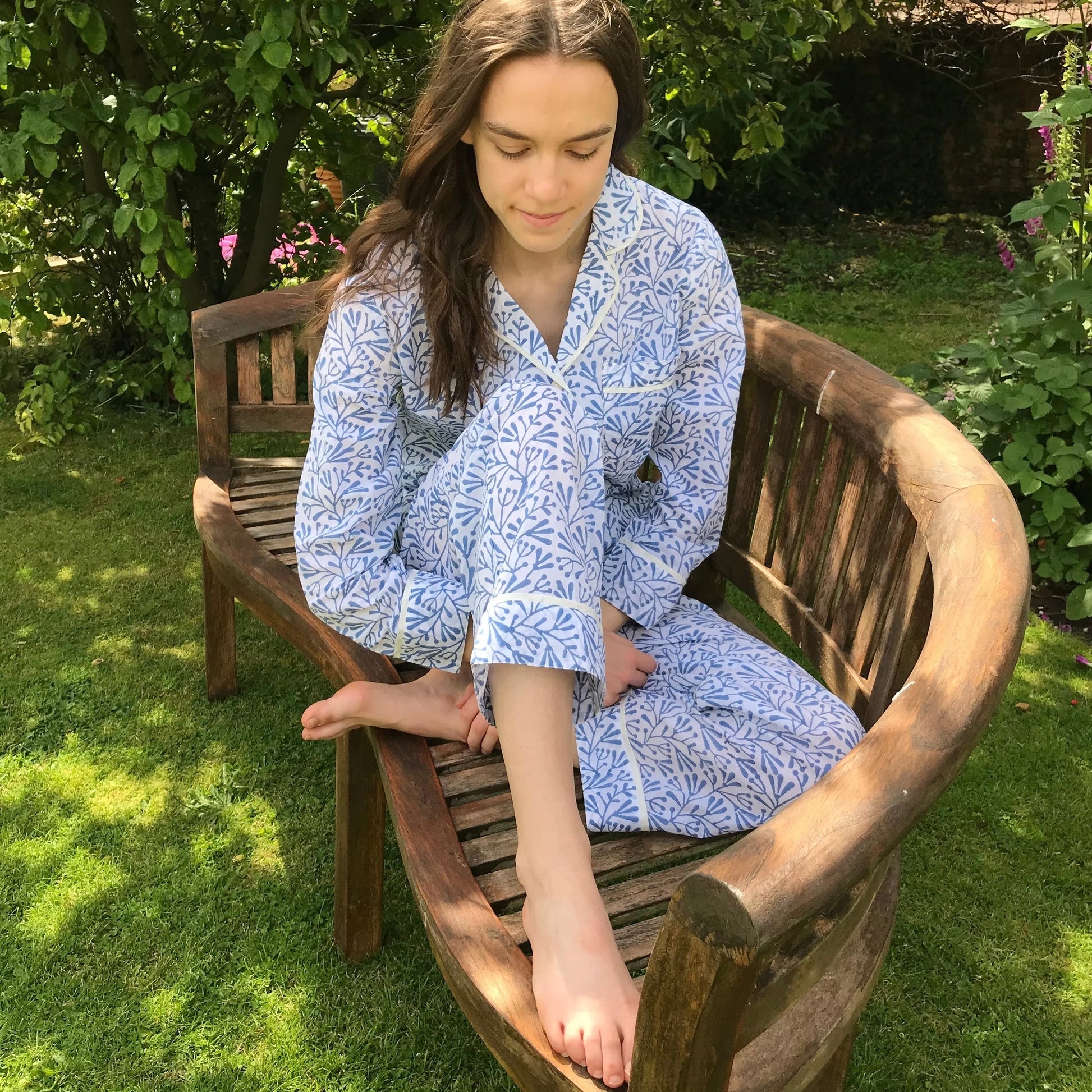 Woman in a blue patterned robe sitting on a wooden bench in a garden.
