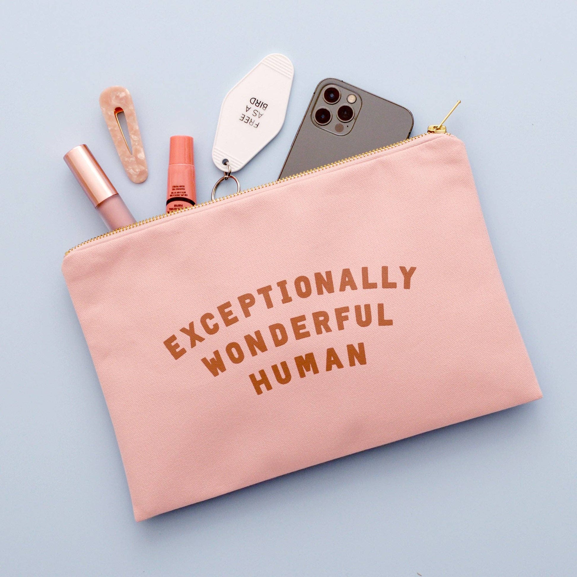Pink pouch with 'Exceptionally Wonderful Human' text, containing a phone, lip gloss, and other items on a light blue background.