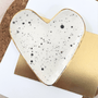 Heart-shaped ceramic dish with speckled design and gold rim on a white background