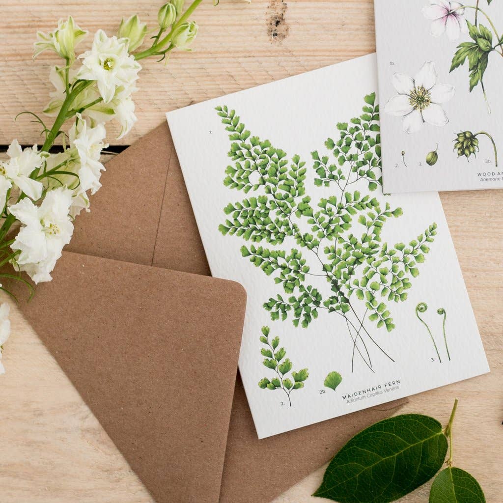 Greeting card with green leaf design on a wooden surface with flowers and an envelope.