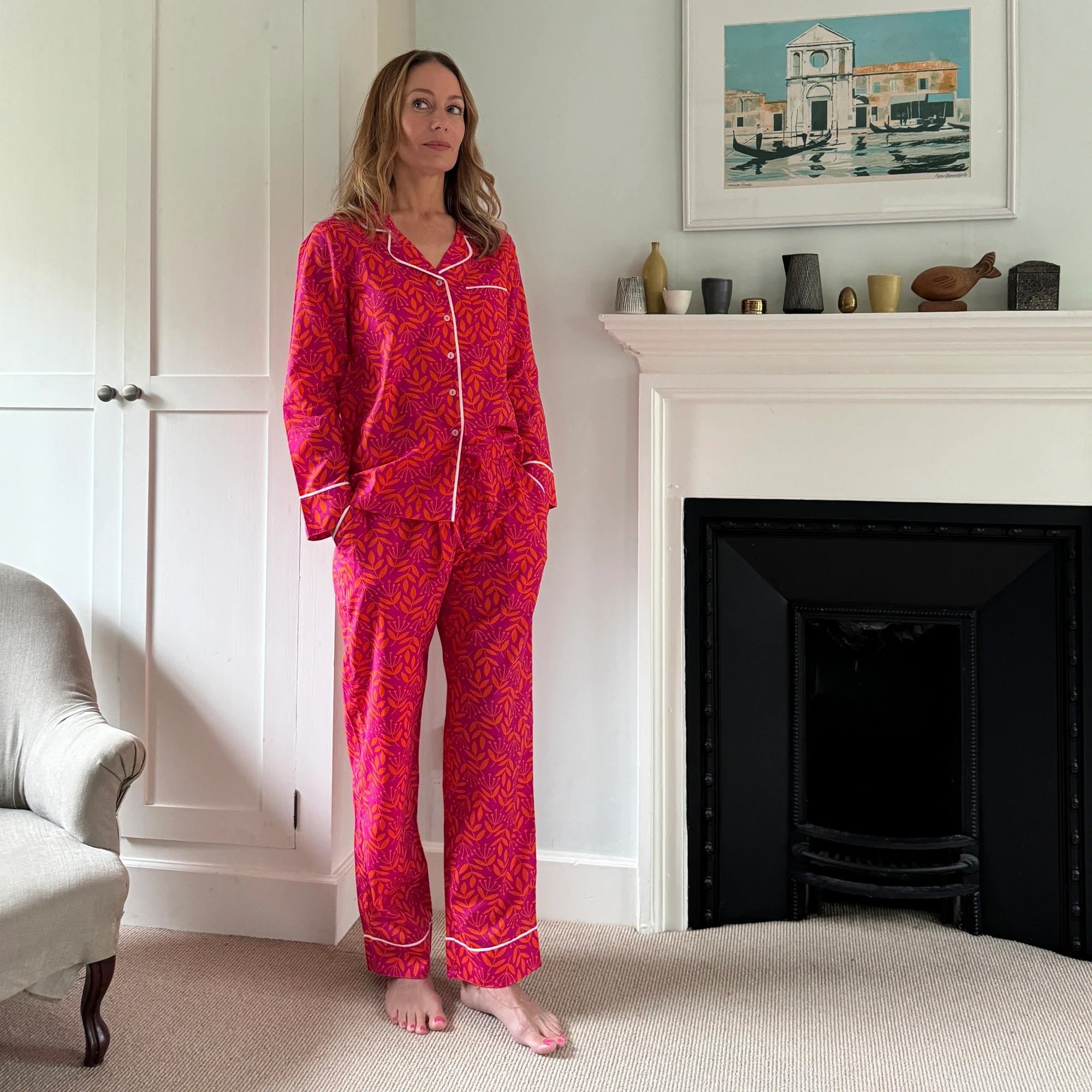 Woman wearing red patterned pajamas standing in a room with a fireplace and decorative items.