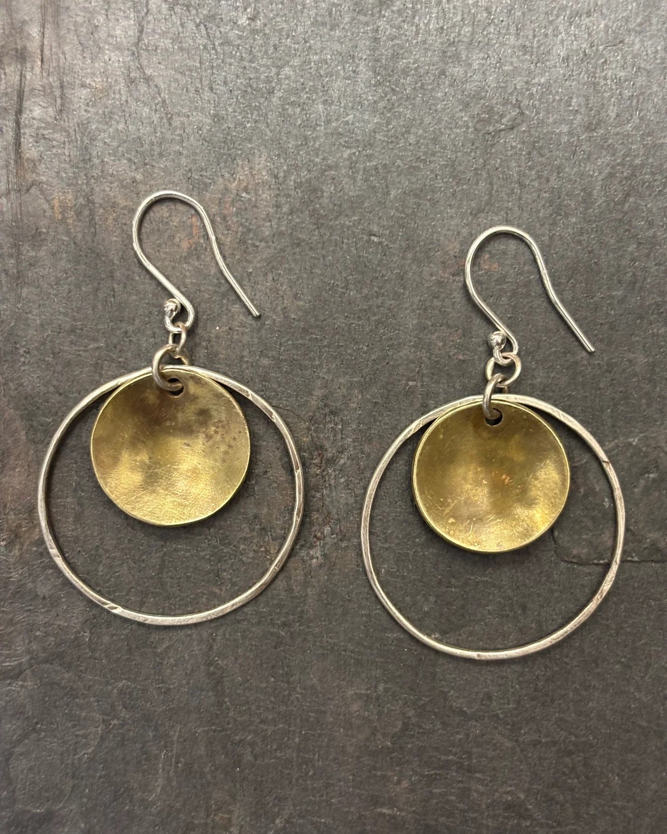 Pair of earrings with gold disc and silver hoop design on a dark surface