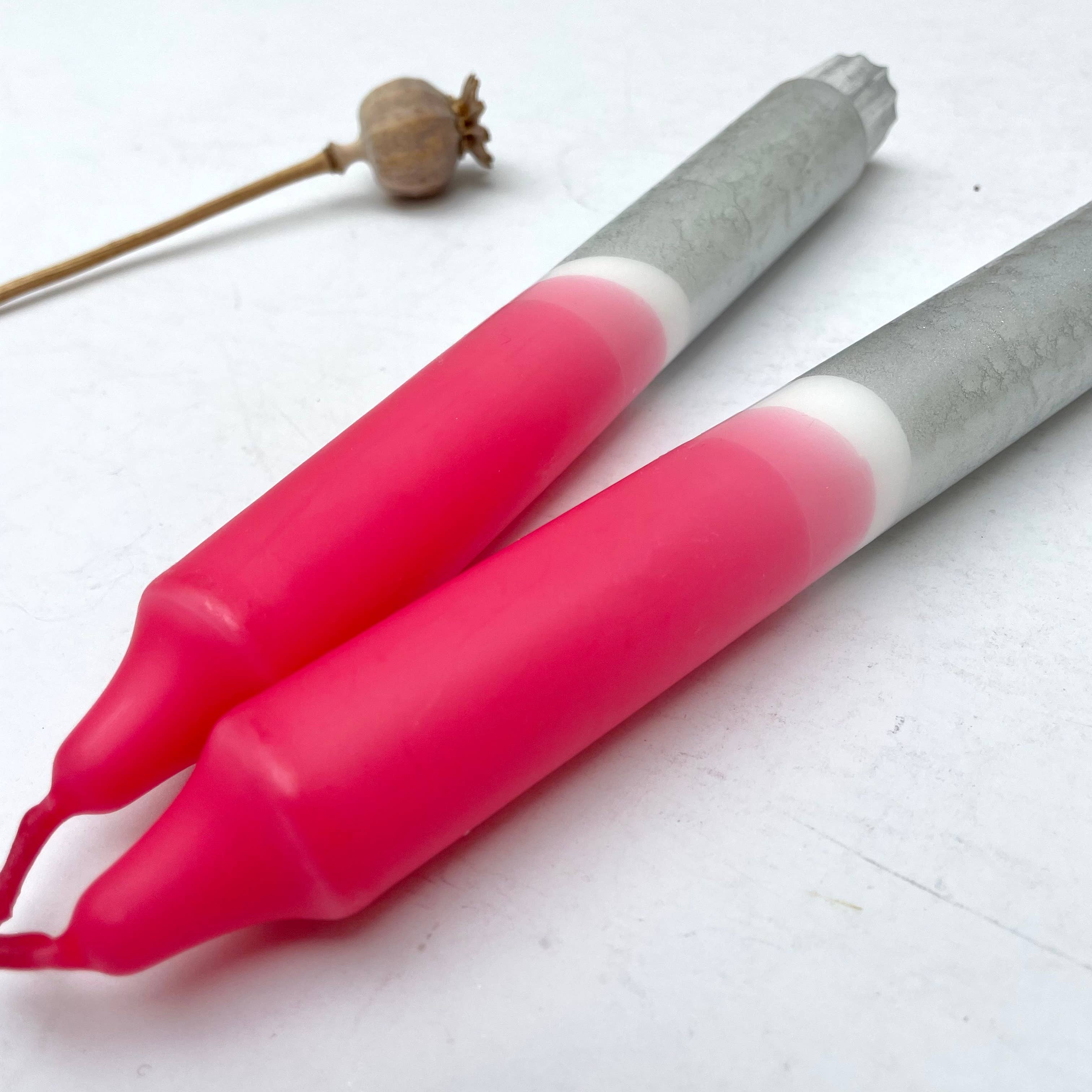 Two pink and gray tools on a white surface with a dried plant in the background.