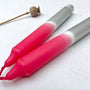 Two pink and gray tools on a white surface with a dried plant in the background.