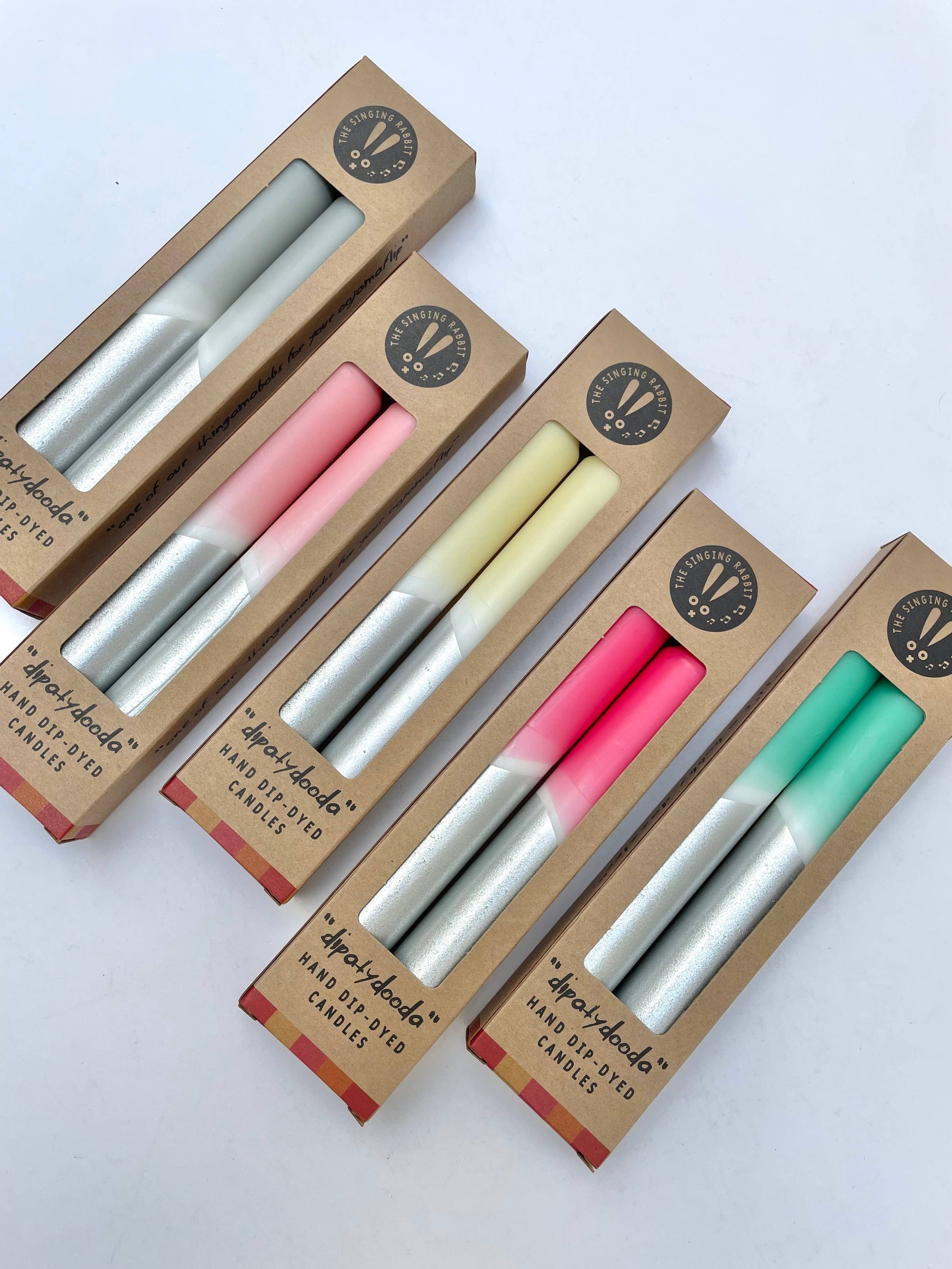Set of four candles in different colors with cardboard packaging on a white background