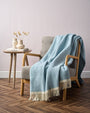 Light blue throw blanket draped over a chair in a room with a side table and decor.