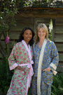 Two women wearing floral robes standing outdoors with a wooden cabin in the background.