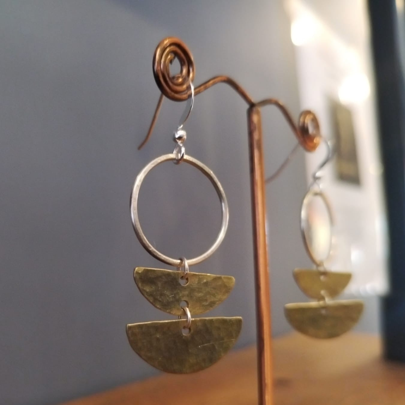 Gold hoop earrings with geometric designs on a stand against a neutral background