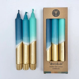 Set of gradient candles with gold and blue finish next to their packaging on a light gray background