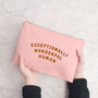 Pink pouch with 'Exceptionally Wonderful Human' text held by a person on a light gray background
