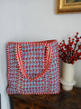 Red and blue patterned bag on a wooden surface with a vase of red berries in the background.