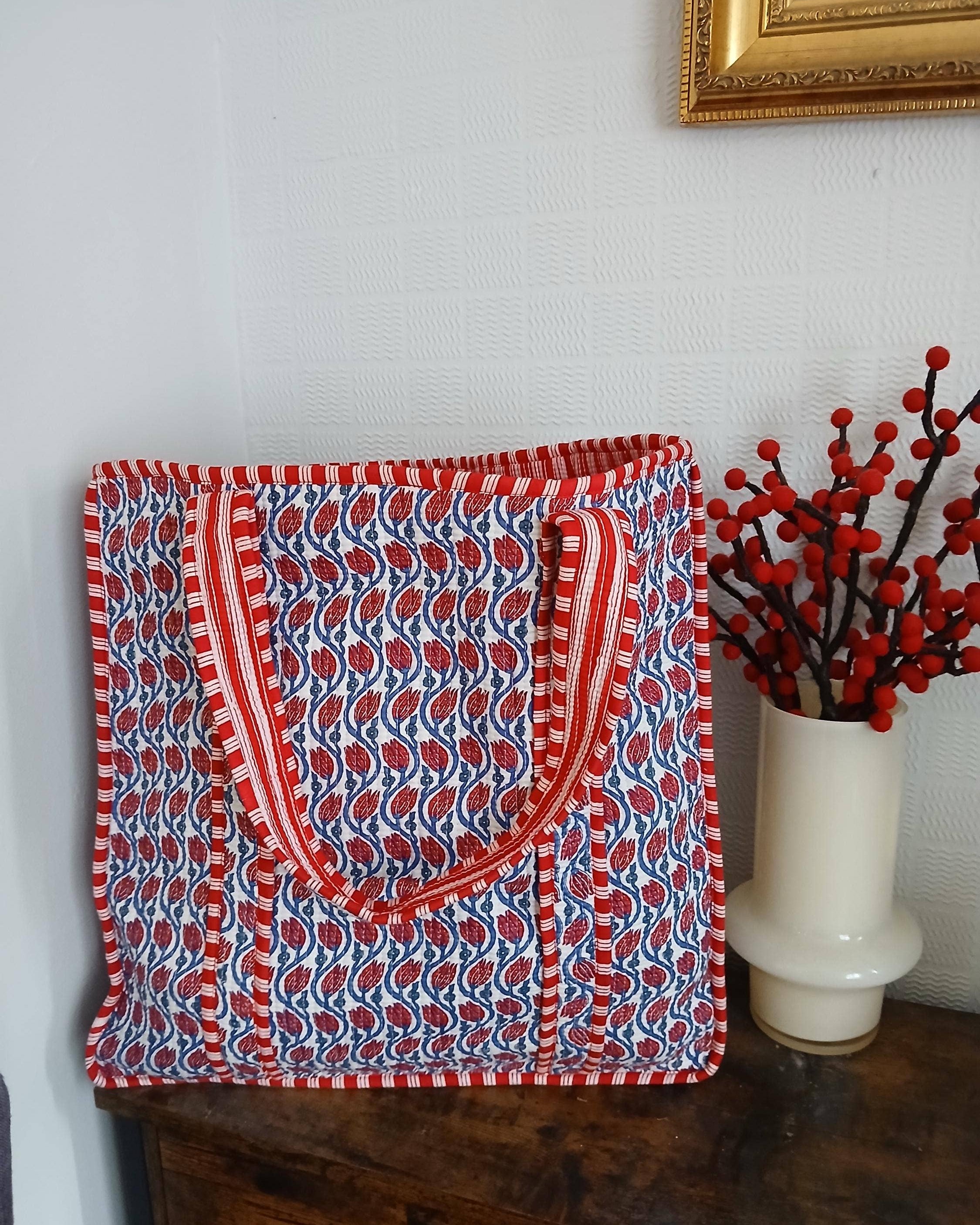 Red and blue patterned bag on a wooden surface with a vase of red berries in the background.