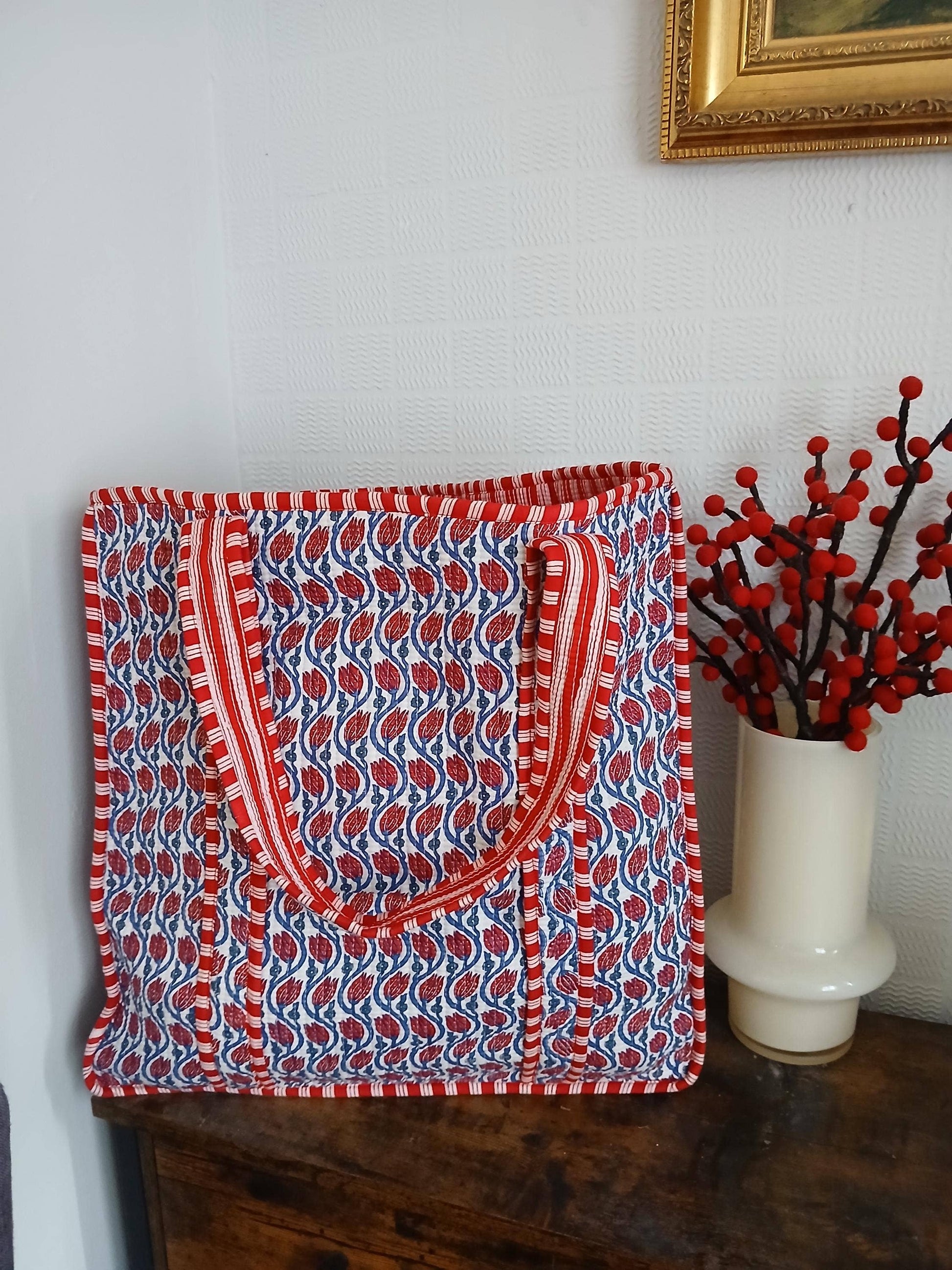 Red and blue patterned bag on a wooden surface with a vase of red berries in the background.