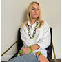 Woman wearing a white shirt with green and black accessories sitting on a chair.