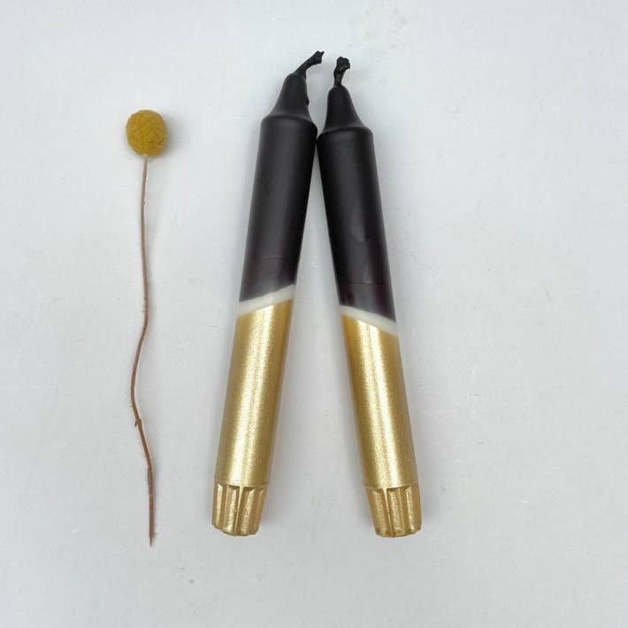 Two black and gold markers with a small yellow object on a white background